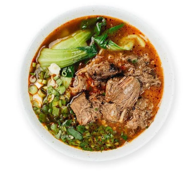 Spicy beef noodle soup with beef chunks, bok choy and chopped green herbs