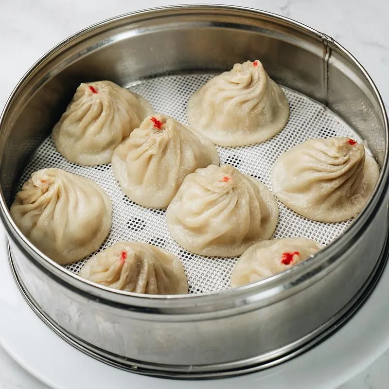 Steamed soup dumplings with red dot marks in metal steamer