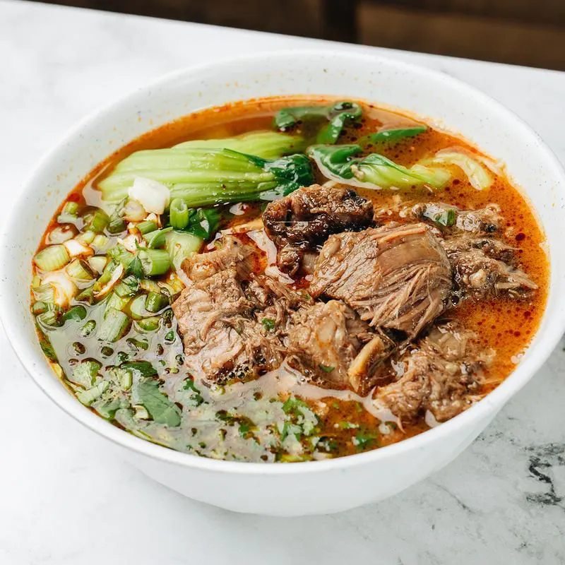 Spicy beef noodle soup with beef chunks, bok choy and herbs