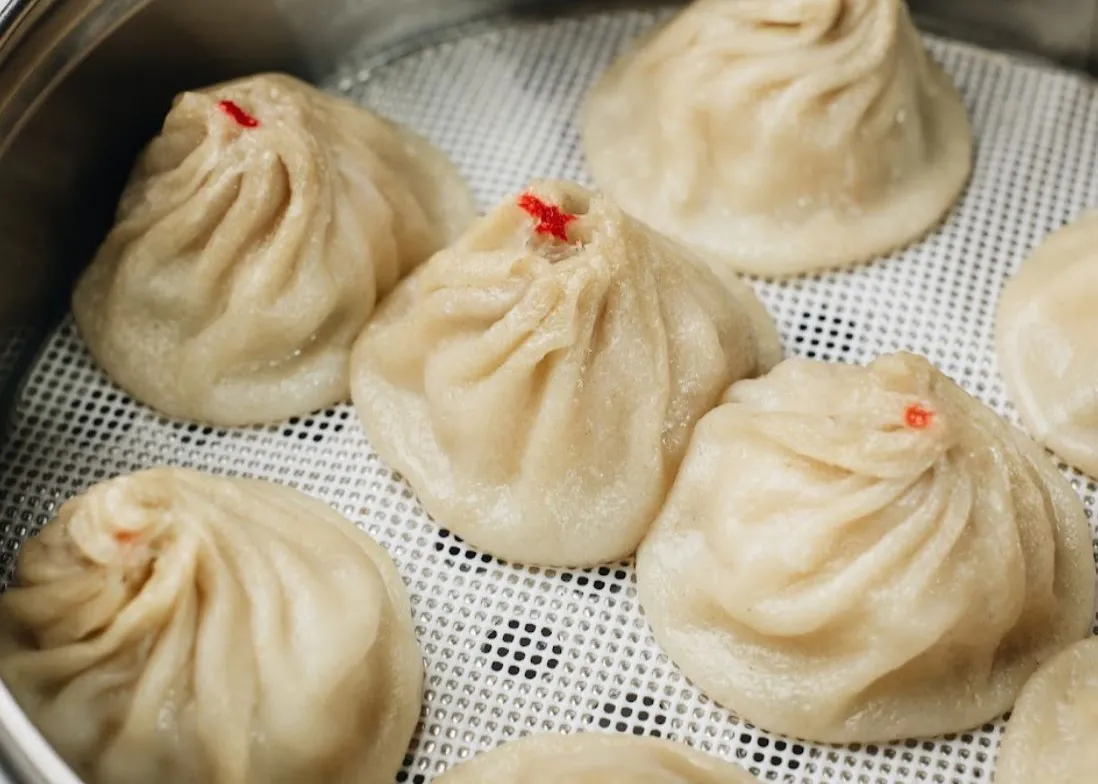 Steamed soup dumplings with red dot on top in metal steamer tray