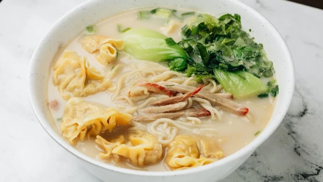 Wonton noodle soup with wontons, bok choy and shredded meat in creamy broth