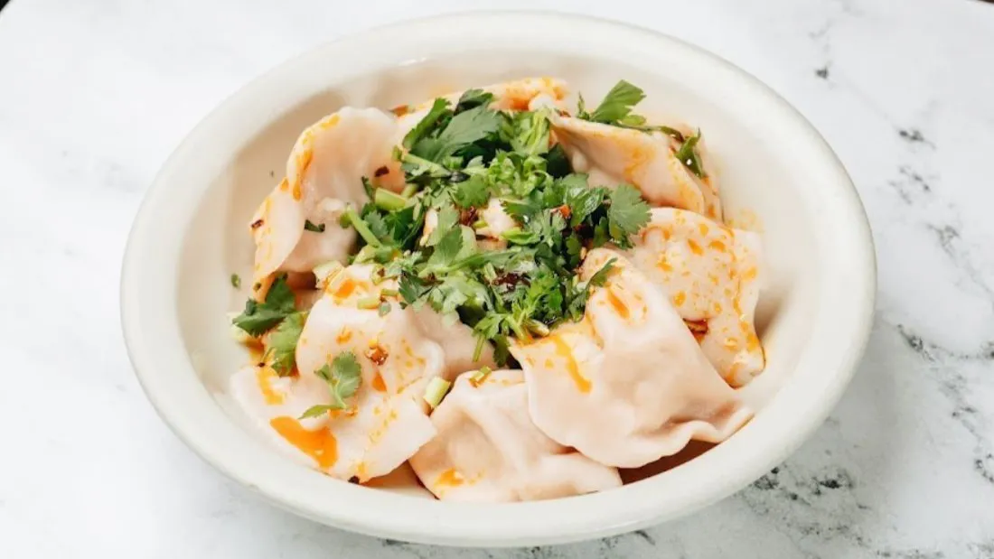 Spicy dumplings topped with fresh cilantro in white bowl